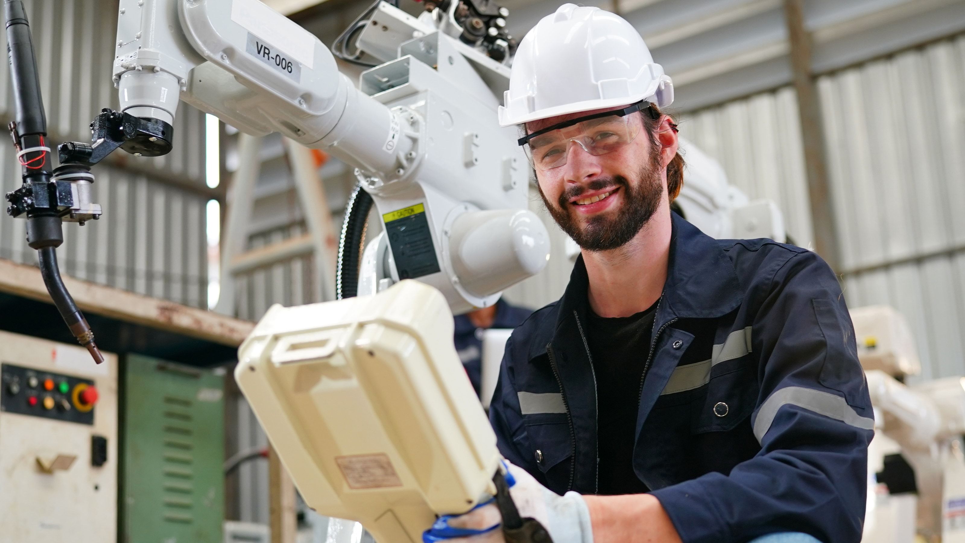 Ingeniero de robótica revisando un robot industrial con la consola de programación en una planta